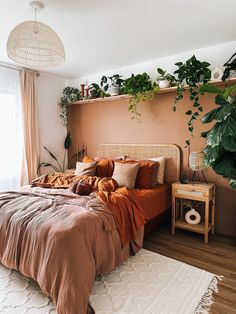 a bed with orange sheets and pillows in a bedroom next to a plant on the wall