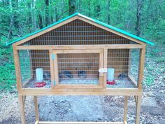 a wooden bird cage with two birds in it and one on the ground next to trees