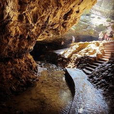 some people are standing in a cave by the water and stairs that lead up to them