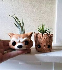 a hand holding a small planter next to a fake raccoon and an air plant