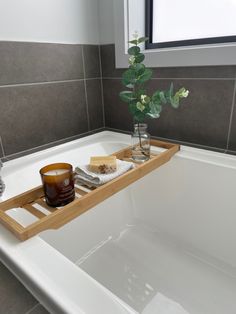 a bath tub with a wooden tray holding soap and a candle on top of it