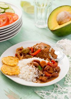 a white plate topped with rice and meat next to sliced avocado on a table