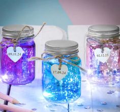 three mason jars filled with blue, purple and pink liquid sitting on top of a table