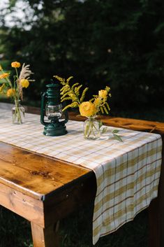 a wooden table topped with vases filled with yellow flowers next to a green lantern