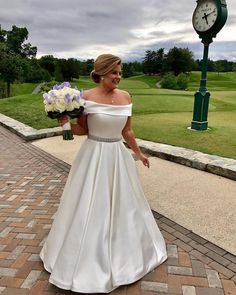 a woman in a white wedding dress walking down a path with flowers and a clock