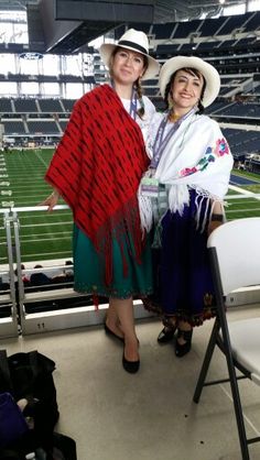 two women standing next to each other in front of a stadium filled with people and chairs