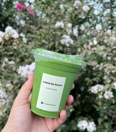 a person holding up a green cup in front of some bushes and flowers with the words starbucks house written on it