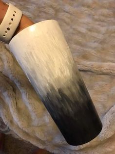 a hand holding a white and black cup on top of a bed