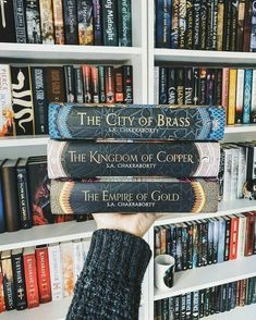 a person holding up three books in front of a book shelf filled with many books