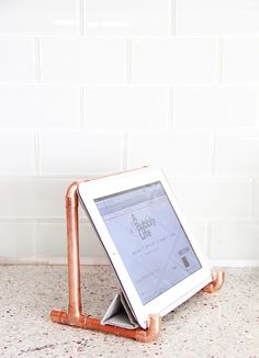 an ipad sitting on top of a copper pipe holder in front of a white brick wall