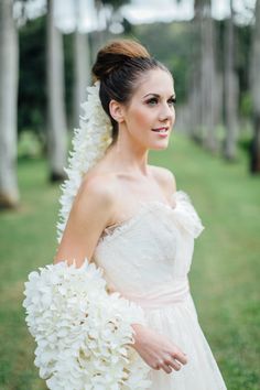 a woman in a wedding dress holding a bouquet of white flowers on her shoulder and smiling at the camera