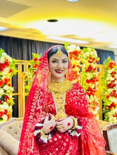 a woman in a red and gold bridal outfit standing next to a flower arrangement