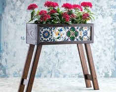 a planter with red flowers in it sitting on a wooden stand next to a wall