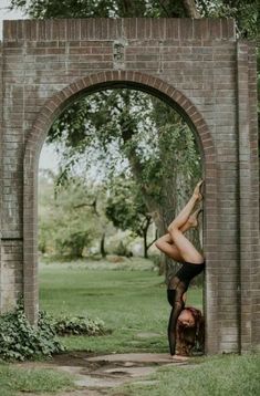 a woman doing a handstand in front of a brick arch on the grass