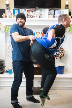 two men are dancing in front of a fireplace with the man holding on to his leg