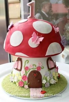 a mushroom shaped cake on top of a white plate with pink flowers and butterflies around it