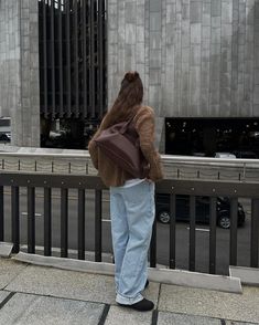 a person standing on the sidewalk with a backpack over their shoulder, looking at something