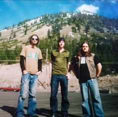 three young men standing next to each other in front of a mountain with trees on it