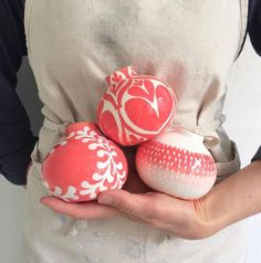 the woman is holding three painted eggs in her hands and she has an apron over her shoulder