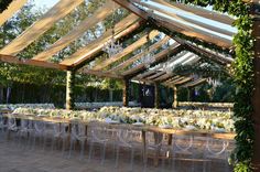 an outdoor dining area with clear chairs and white tablecloths on the long tables