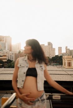 a pregnant woman standing on top of a roof with buildings in the backgroud