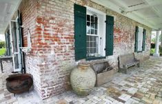 an old brick house with green shutters on the front door and windows, along with two wooden benches