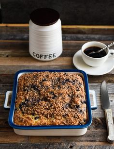 a blue casserole sitting on top of a wooden table next to a cup of coffee