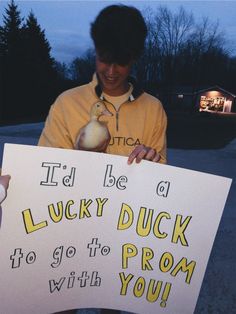 a man holding up a sign with a duck on it's chest and the words i'd be a lucky duck to go to prom with you