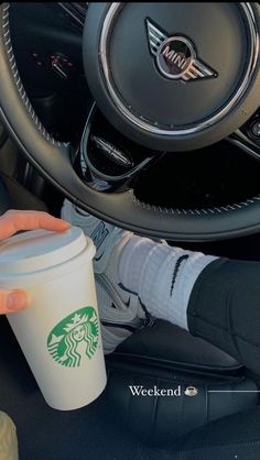 a person holding a starbucks cup in their hand while sitting in the driver's seat of a car