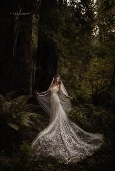 a woman in a white wedding dress standing in the woods with her veil flying over her head