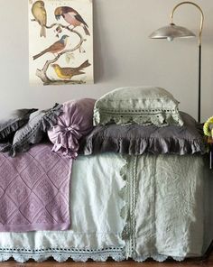 a bed with purple and green sheets in a bedroom next to a painting on the wall