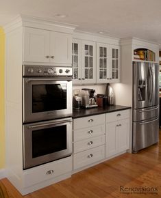 a kitchen with white cabinets and stainless steel appliances in the center, along with hardwood flooring