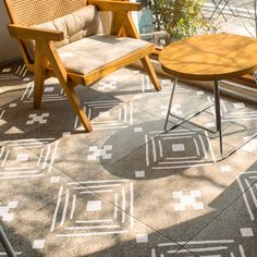 two wooden chairs sitting on top of a cement floor next to a table and potted plant