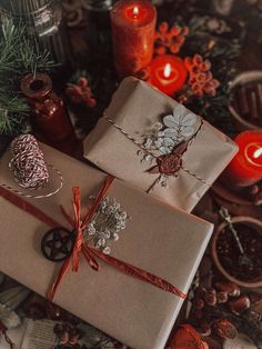 two wrapped presents sitting on top of a table next to candles and pine cones,