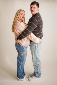 a man and woman standing next to each other with their arms around each other in front of a white background