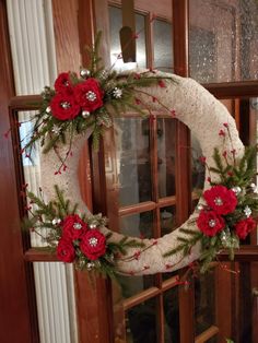 a white wreath with red flowers and greenery hanging from the side of a door