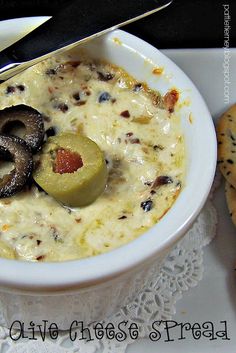 a white bowl filled with food next to crackers and a knife on top of a doily