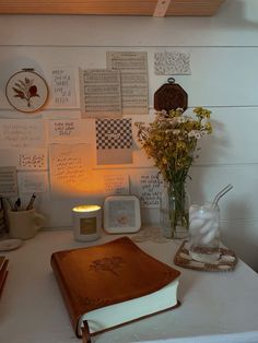 a table topped with a book and vase filled with flowers next to a candle on top of a white counter