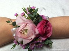 a wrist corsage with pink flowers and greenery on the arm for decoration