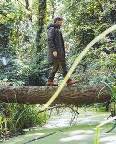 a man walking across a fallen tree in the woods