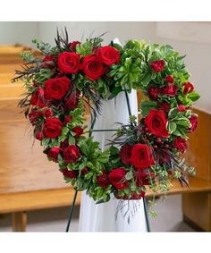 a wreath with red roses and greenery on it in front of a church pew