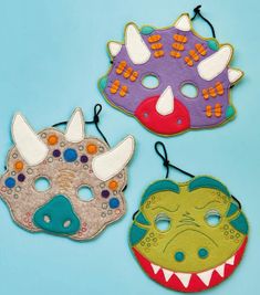 three masks with different designs on them are hanging from strings in front of a blue background