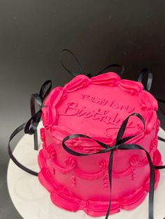 a pink birthday cake with black ribbon on top