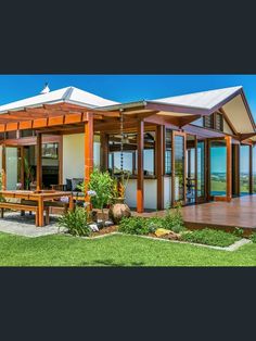 an outdoor living area with wooden furniture and large windows on the side of the house