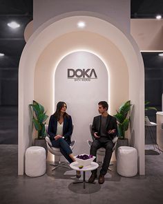 two people sitting on chairs in front of a doka sign at an exhibit booth