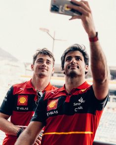 two men standing next to each other in front of a stadium holding up a cell phone