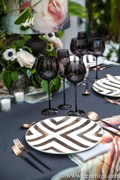 the table is set with black and white plates, silverware, and flowers in vases