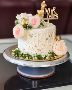 a white cake with flowers and a gold topper sitting on a silver platter