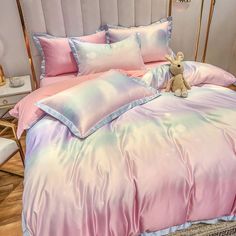 a bed with pink and blue comforters, pillows and a teddy bear on it