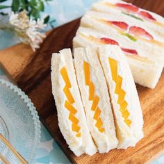 small sandwiches are on a wooden cutting board next to flowers and chopsticks in front of them